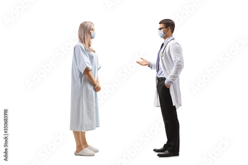 Female patient in a hospital gown and a male doctor talking and wearing protective masks
