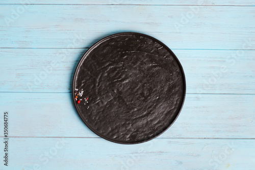 Top view of dark ceramic plate with spice and salt on a light blue wooden background.