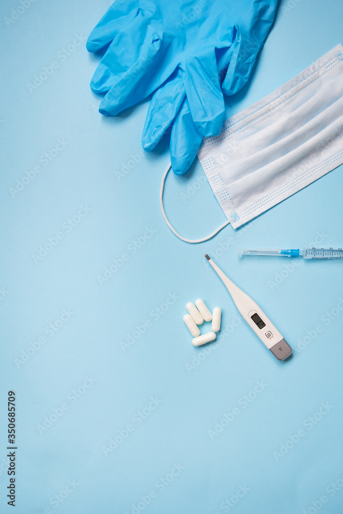 Blue latex gloves on a blue background lie with pills, medical mask, thermometer and syringe Blue latex gloves on a blue background lie with pills, medical mask, thermometer and syringe