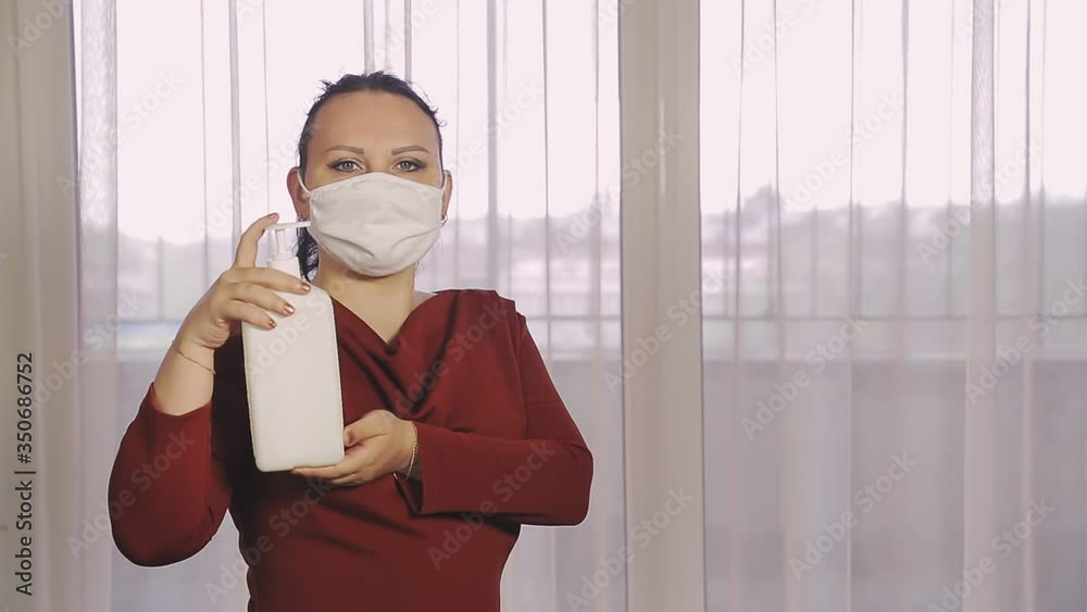 A woman in a public place in a protective mask disinfects her hands with a professional antiseptic
