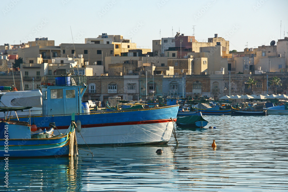 Barcos amarrados en un puerto pesquero de Malta, al fondo se ven las casas del pueblo