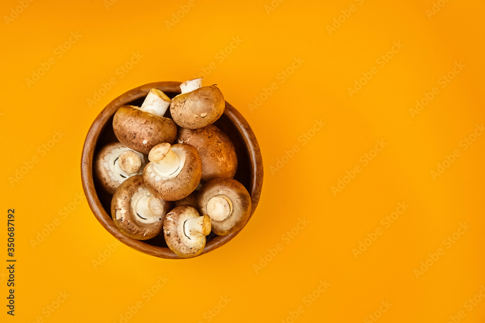 Mushrooms in wooden bowl, fresh brown champignons on a yellow background with copy space, top view Mushrooms in wooden bowl, fresh brown champignons on a yellow background with copy space, top view
