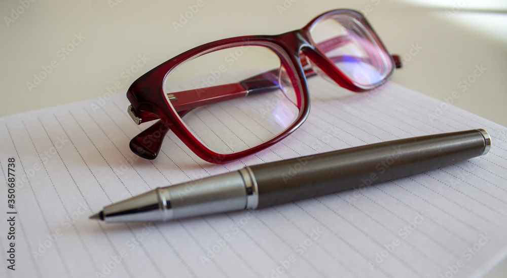 Metal pen on white note and beautiful glasses on a white table. Business concept. Metal pen on white note and beautiful glasses on a white table. Business concept.