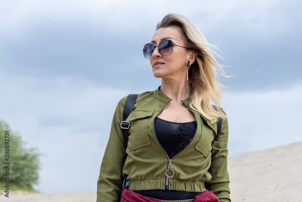Portrait of an adult woman in sunglasses and military style clothes on a blue sky background. Portrait of an adult woman in sunglasses and military style clothes on a blue sky background.