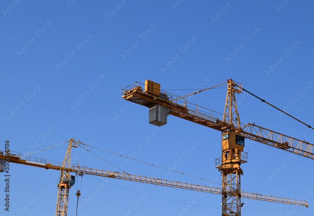 Two large, yellow cranes with a blue, cloudless sky. Two large, yellow cranes with a blue, cloudless sky.