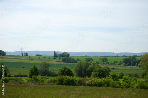 Hügelige Landschaft mit Hecken, Bäume, Strommasten, Wiesen, Feldern, befahrener Straße und Baustelle im Sommer