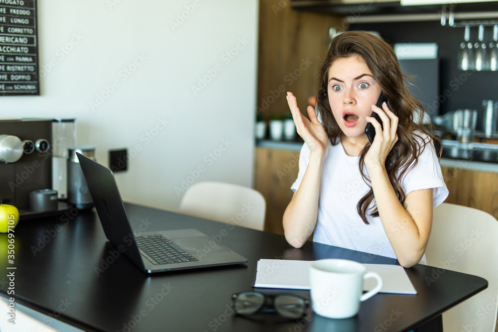 Beautiful shocked girl is talking on the mobile phone, using a laptop and smiling at home Beautiful shocked girl is talking on the mobile phone, using a laptop and smiling at home