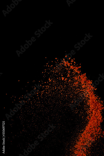 Red paprika spices powder explosion, flying chili pepper isolated on black background. Splash of spice background. photo