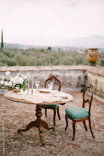 A wooden table and two antique chairs, served and decorated for a wedding dinner.