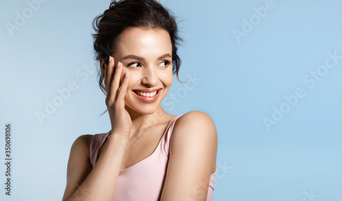 Young woman with bare shoulder and shiny glowing perfect face skin laughing timid. 