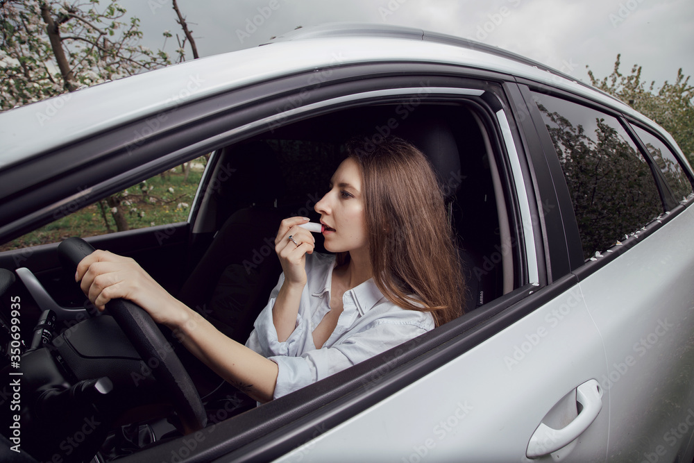 Young woman driving a car. The girl paints her lips in the car. Woman doing makeup in the car.