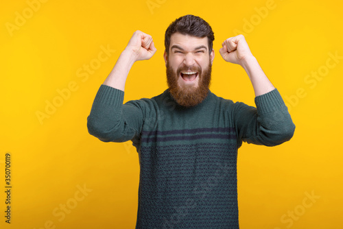 bearded man is making the winner gesture on yellow background.