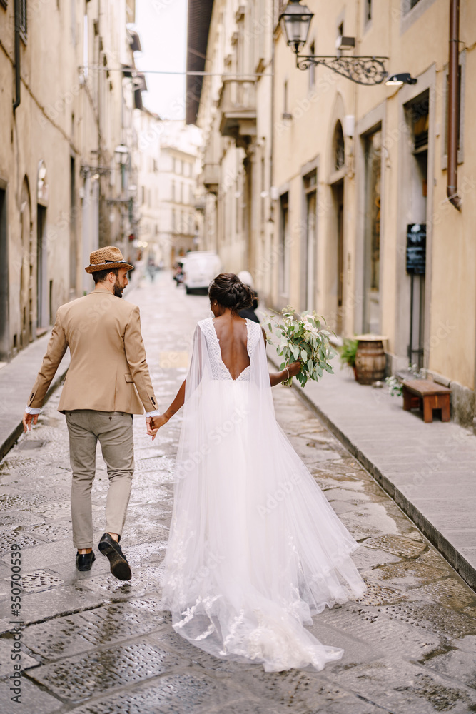 Interracial wedding couple. Wedding in Florence, Italy. African-American bride and Caucasian groom walk down the street.