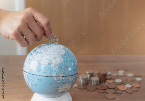 Business woman hand putting one pound coin in to glob bank for donate money helping the earth, People saving money for the future or traveling around the world concept.