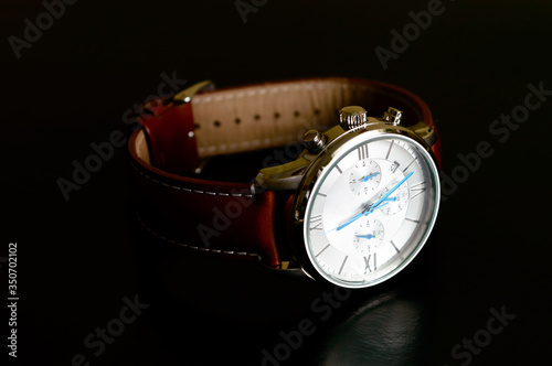 Nice luxury man's wrist watch with blue clock hands and brown leather strap on black background