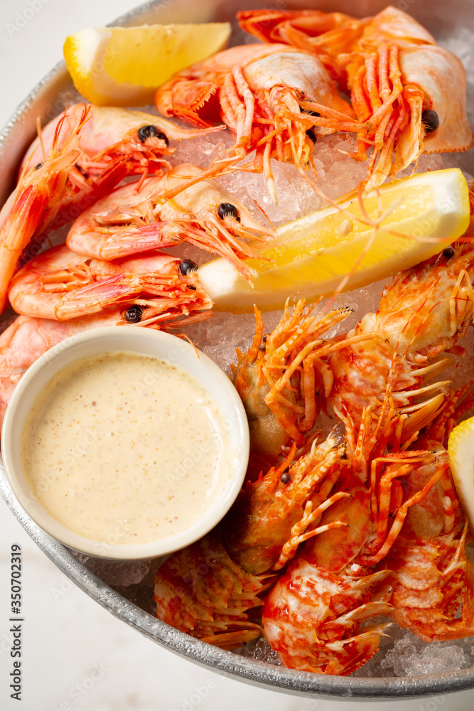 Freshly cooked assorted shrimps on the ice plate with lemon slices and sauces on a stone countertop. Freshly cooked assorted shrimps on the ice plate with lemon slices and sauces on a stone countertop.