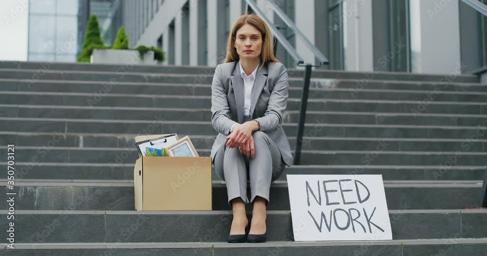 Portrait of young workless Caucasian woman office worker sitting on stairs outdoors with carton table Need Work. Unemployment after pandemic lockdown. Workless fired female. Portrait of young workless Caucasian woman office worker sitting on stairs outdoors with carton table Need Work. Unemployment after pandemic lockdown. Workless fired female.