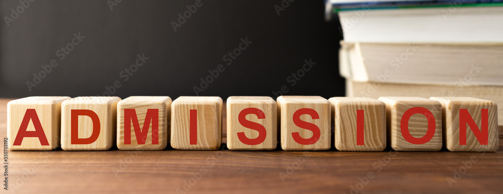 ADMISSION word written on wooden cubes on the backround of stack of books. Education, business concept ADMISSION word written on wooden cubes on the backround of stack of books. Education, business concept