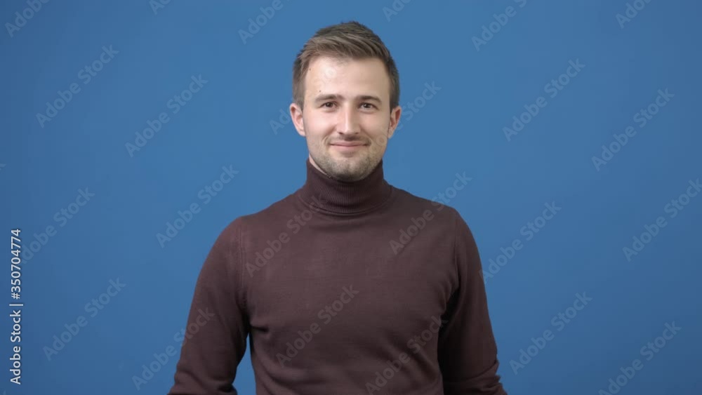 Happy attractive charismatic young man raising palm to wave friendly to welcome ans say hello, smiling broadly showing hi gesture being nice to guest over blue background