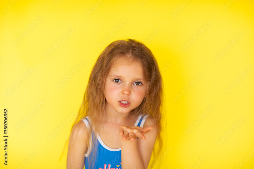 Little girl with brown hair in blue swimsuit posing on yellow background Little girl with brown hair in blue swimsuit posing on yellow background