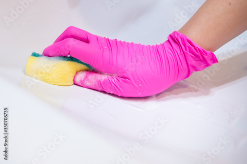 A hand in a pink glove washes a washbasin in the bathroom with a sponge with foaming detergent. Cleaning company cleans the house. Disinfection of the senile node from viruses and bacteria.