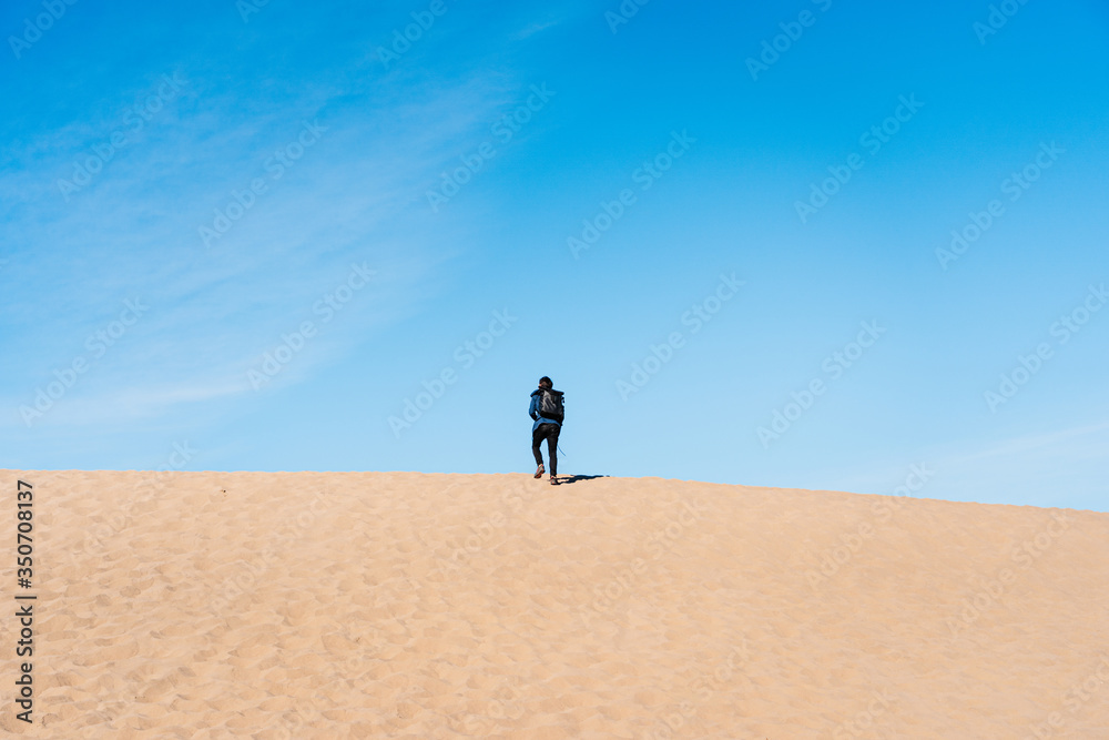 A traveling man is going on the top of a sand dune. A traveler in a black skirt in Death Valley National Park