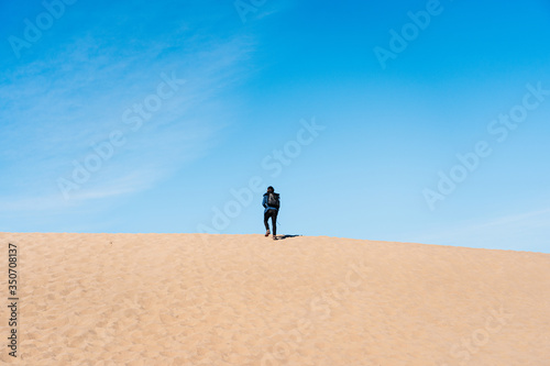 A traveling man is going on the top of a sand dune. A traveler in a black skirt in Death Valley National Park