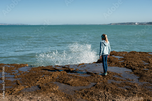 Tween girl watching waves splash over rocks in New Zealand