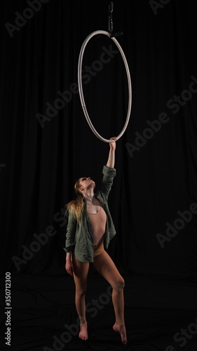 Beautiful graceful girl, aerialist. professional circus acrobat on an aerial hoop. performer holding a ring in his hands, black background. black curtain backstage with pleats, rehearsal, grace.