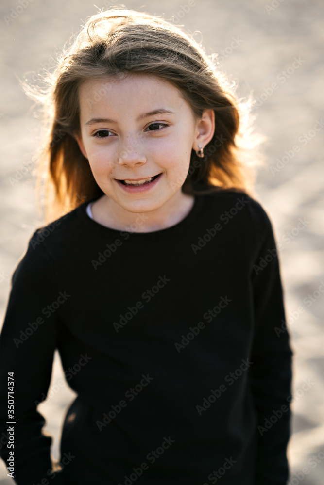 Portrait of a cheerful little girl on the beach at sunset. Kid girl having fun in holiday vacation. Youth, lifestyle and happiness concept. Portrait of a cheerful little girl on the beach at sunset. Kid girl having fun in holiday vacation. Youth, lifestyle and happiness concept.