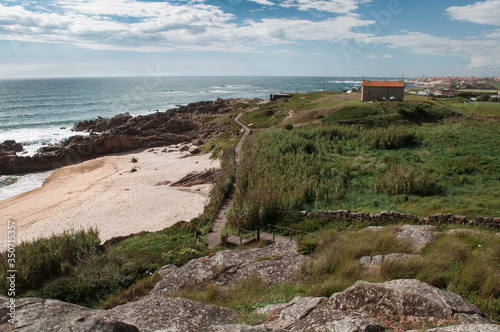 The landscape, the panorama of the ocean, the beach and the coast, covered with green grass. A small stone church with a red roof on the oceanfront