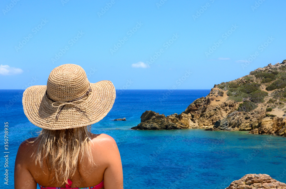 Young girl with straw hat looking at the sea.