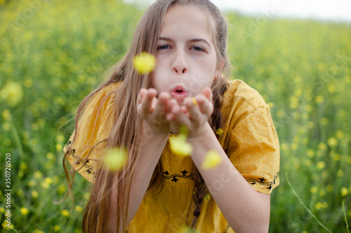 Beautiful Young Girl Blowing Kisses and Flowers (Dandelions) In a Field photo