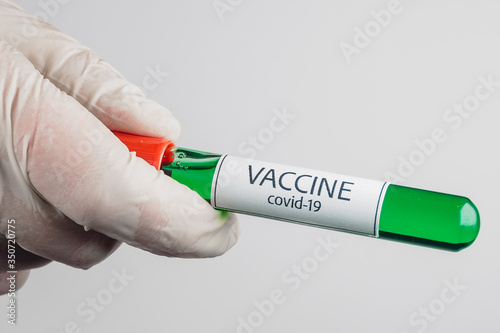 Vacuum tube with a sample of Covid-19 vaccine of green color in the hand with a medical glove on a white background