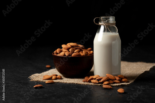 one bottle of almond milk on a dark black background with nuts  vegetarian milk without sugar and lactose