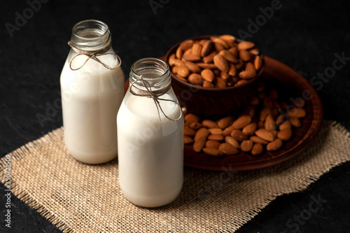 almond milk without sugar and lactose in bottles with sprinkled nuts  vegetarian milk drink on a black table