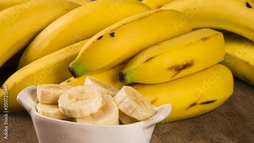 Two bunches of bananas and a sliced banana in a pot over a table.