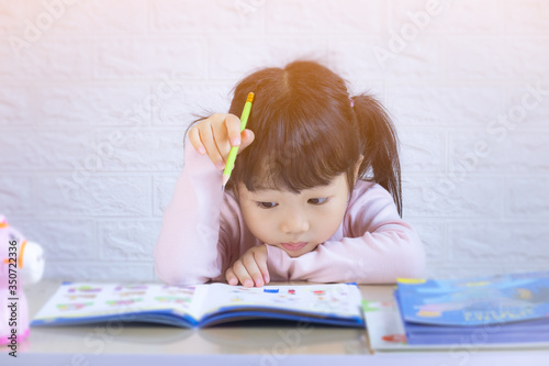 Cute little girl doing homework, reading a book, coloring pages, writing and painting. Children paint. Kids draw. Preschooler with books at home. Preschoolers learn to write and read. Creative toddler