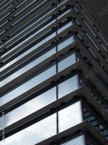 corner view of a modern futuristic office building with blue sky and clouds reflected in the glass