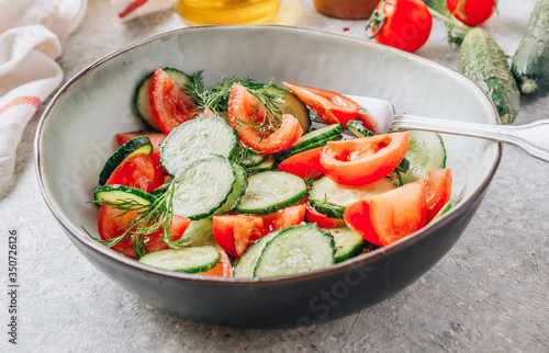 Healthy vegetable salad of fresh tomato, cucumber, dill and spices and oil in bowl on light gray background. Diet concept.