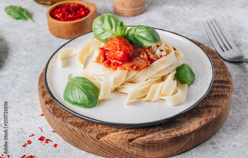 Pasta Tagliatelle Bolognese with meat tomato sauce and fresh basil leaves on white plate and wooden cutting board. Light gray table.
