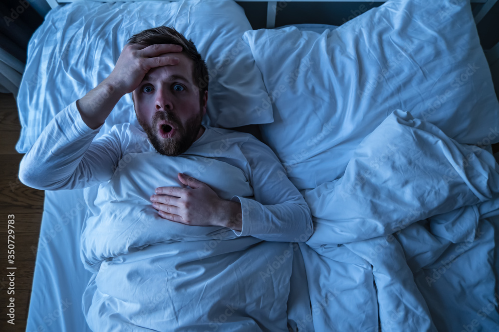 Man had a terrible nightmare, he woke up and looked scared with big eyes.  Concept of insomnia and mental health. Stock Photo | Adobe Stock