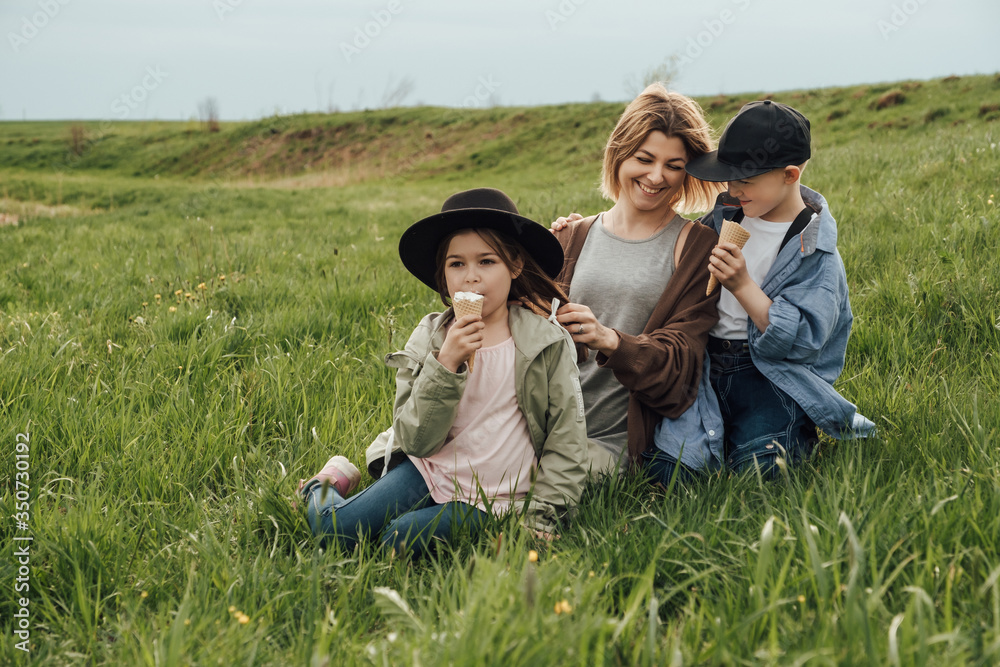 Happy family, mom daughter and son in organic clothes, walk in the field and eat ice cream. The concept of a healthy lifestyle, happiness and joy Happy family, mom daughter and son in organic clothes, walk in the field and eat ice cream. The concept of a healthy lifestyle, happiness and joy