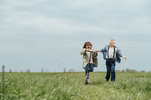 A happy family, mother, daughter and son in organic clothes, walk in the field and ride a scooter. The concept of a healthy lifestyle, happiness and joy