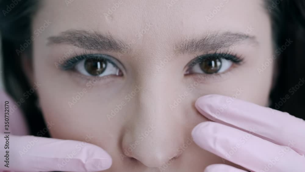 Brunette girl has facial massage. Client is in beauty studio. Masseur wears pink gloves.