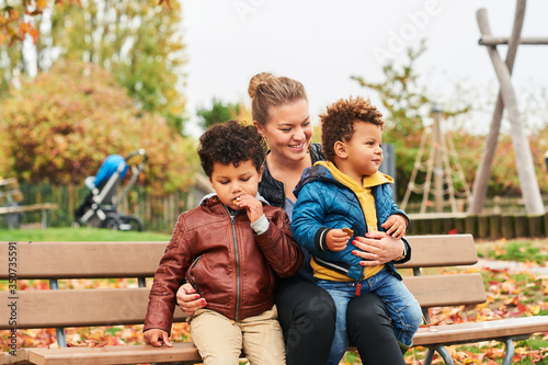 Foto Outdoor portrait of happy young mother with two lovely sons, family enjoying nice autumn day in public park, mixed race family