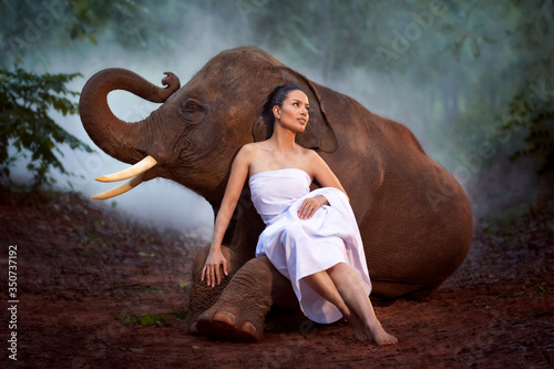The woman priest dressed in white was sitting with an elephant in the deep forest.
