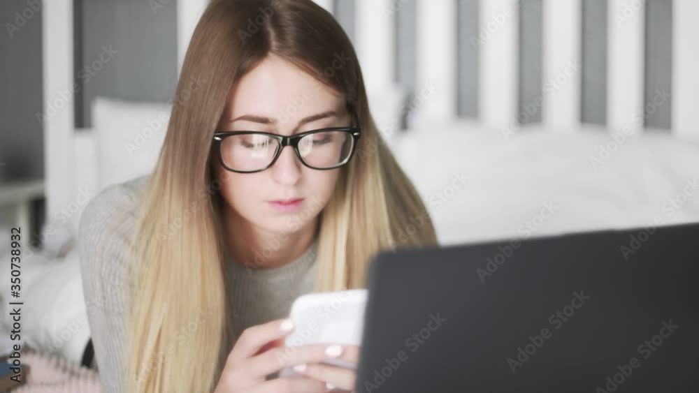 Young woman with galsess lying on the bed and using smartphone Young woman with galsess lying on the bed and using smartphone