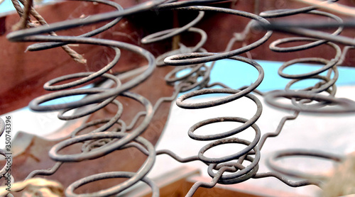 Rusted metal wire chair coils exposed in an antique wooden chair seat.  Rows of metal spirals with jute twine rope. Laid out in an array of pattern.  Chair is a vintage rocker.