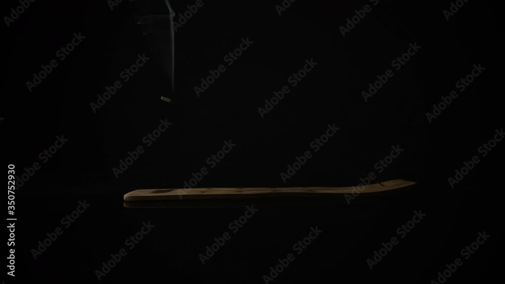 Smoke billows from a stick of incense, burning on a dark black background. Smoke billows from a stick of incense, burning on a dark black background.